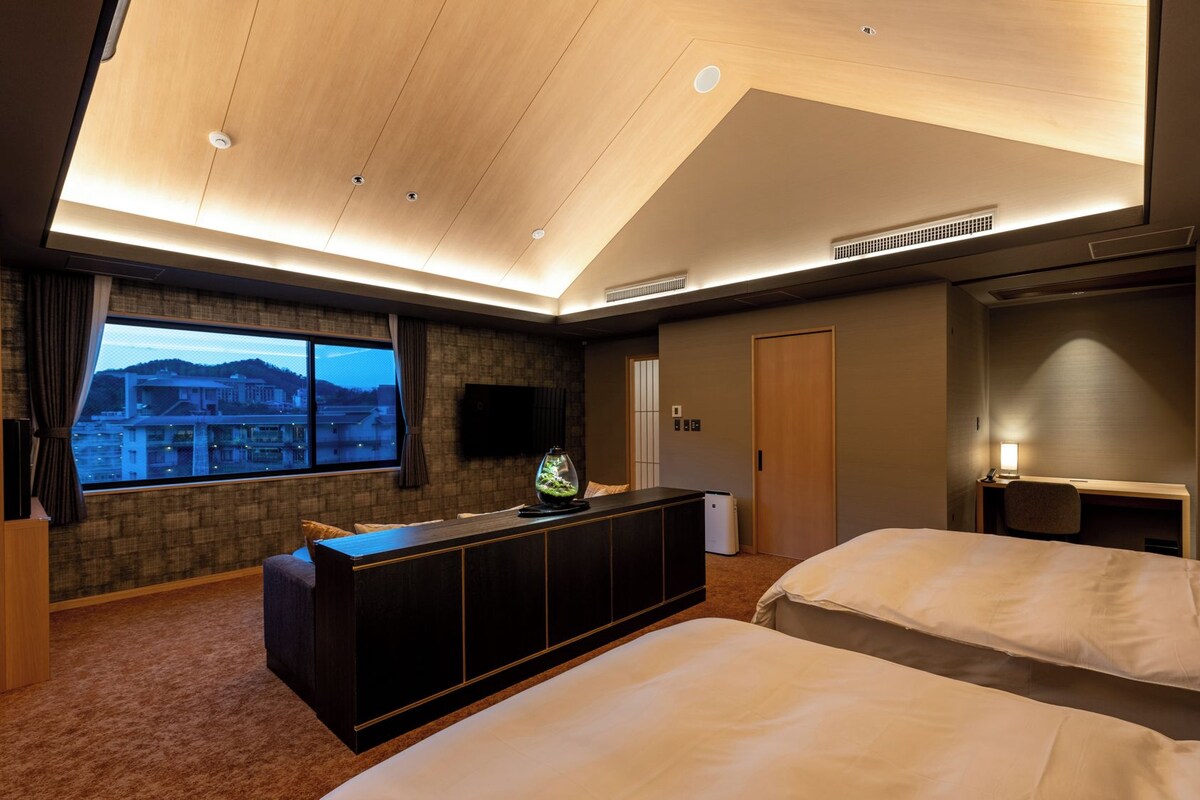 A hotel room with two beds, a large window with a view, a TV, and a minibar.