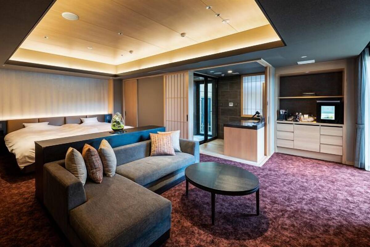 Una habitación de hotel moderna con cama, sofá, escritorio y kitchenette.