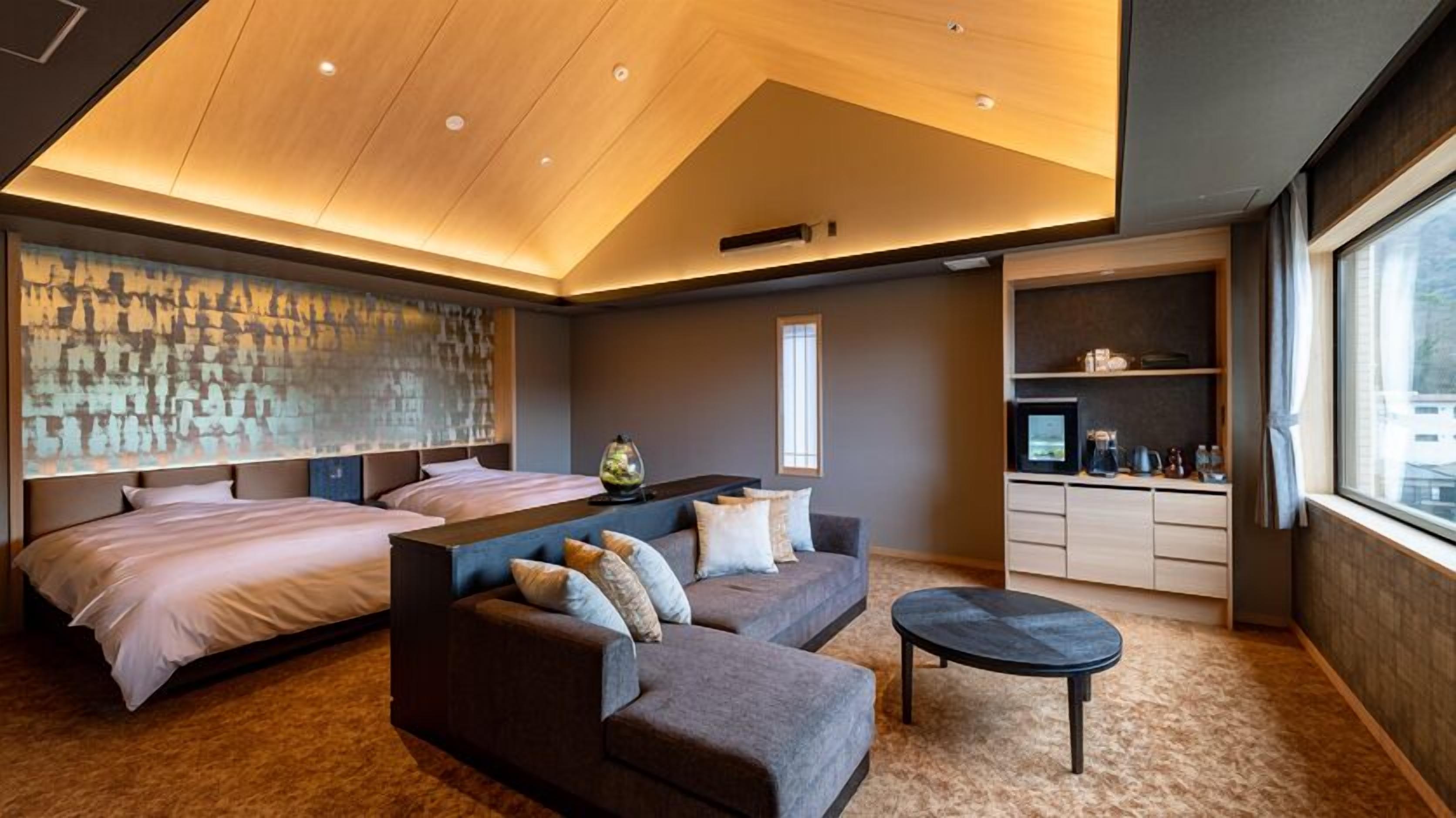 A modern hotel room with a large bed, a sofa, a small table, and a desk with a computer.