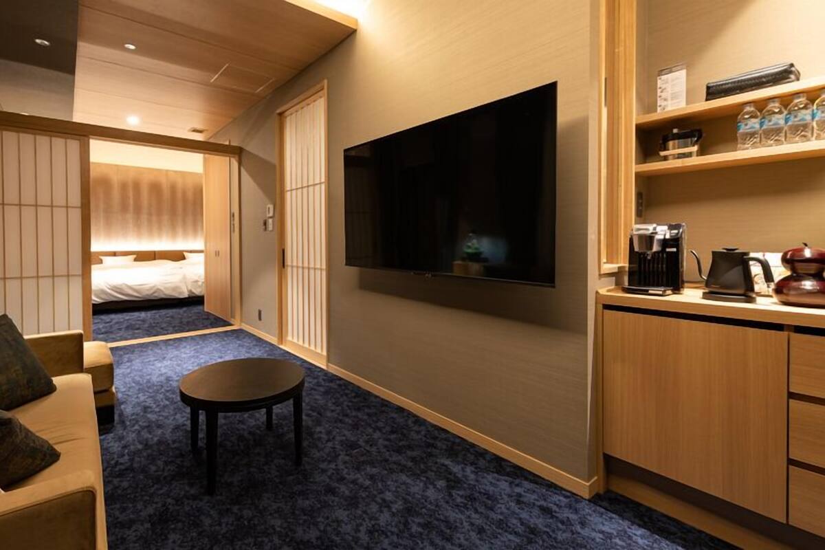 Habitación de hotel con cama, televisión, pequeña mesa, sofá y kitchenette.