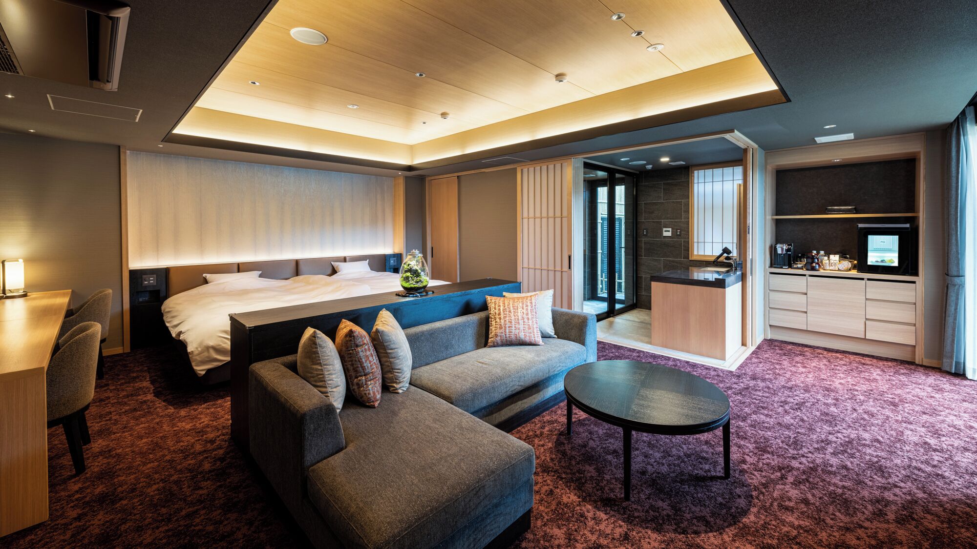 A modern hotel room with a bed, sofa, coffee table, and kitchenette.