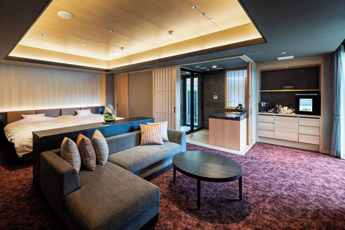 Una habitación de hotel moderna con cama, sofá, mesa de centro y kitchenette.