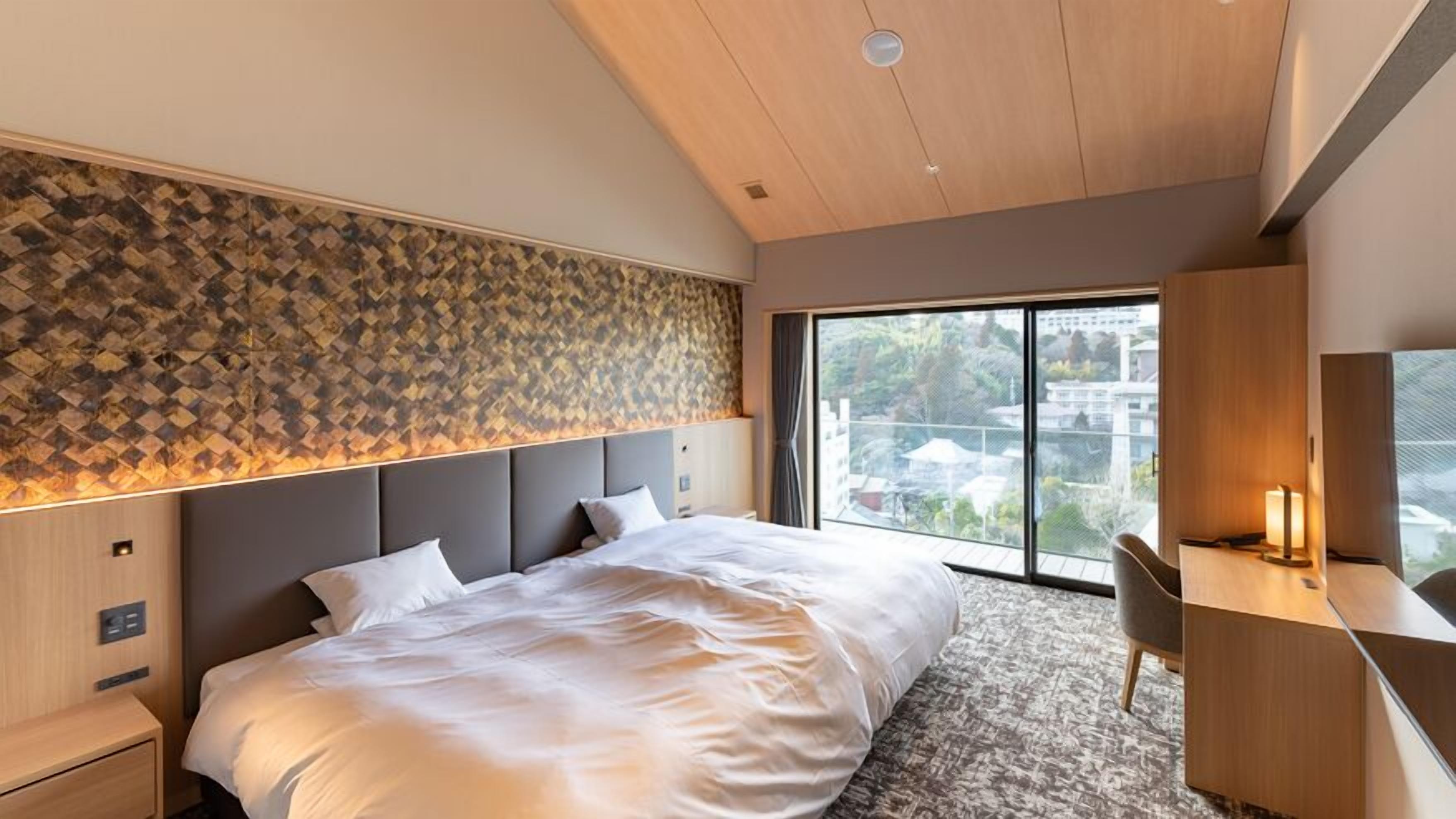 A modern hotel room with a large bed, a desk, and a view of the city.