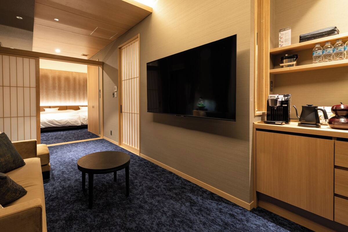 Una habitación de hotel con cama, televisión, una mesita, sofá y kitchenette.