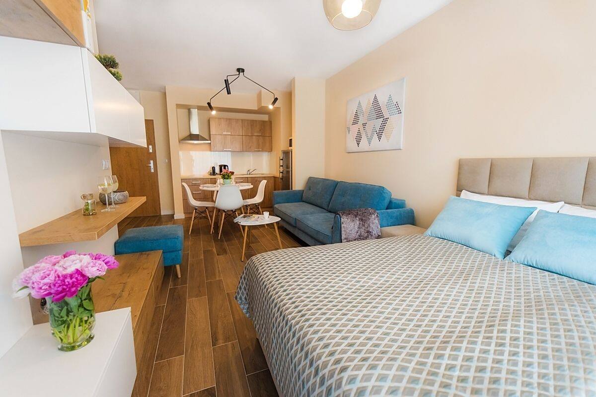 A modern, compact bedroom with a bed, a blue sofa, and a small dining area with a table and chairs.