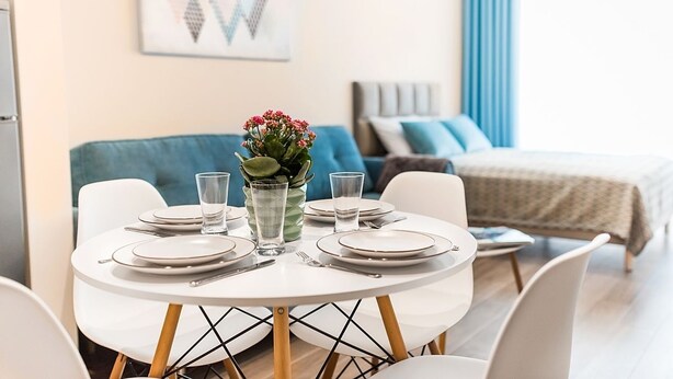 Ein Essbereich mit einem runden Tisch, gedeckt für vier Personen, einer Blumenvase und einem Bett im Hintergrund.