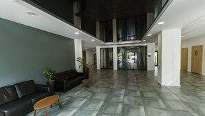 Eine großzügige Lobby mit modernem Design, inklusive einer dunkelgrünen Ledersofa, einem Holztisch und einem Topf mit Pflanze.
