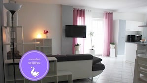 Un salon moderne avec un canapé blanc, un téléviseur à écran plat et un coin cuisine équipé d’un four à micro-ondes.
