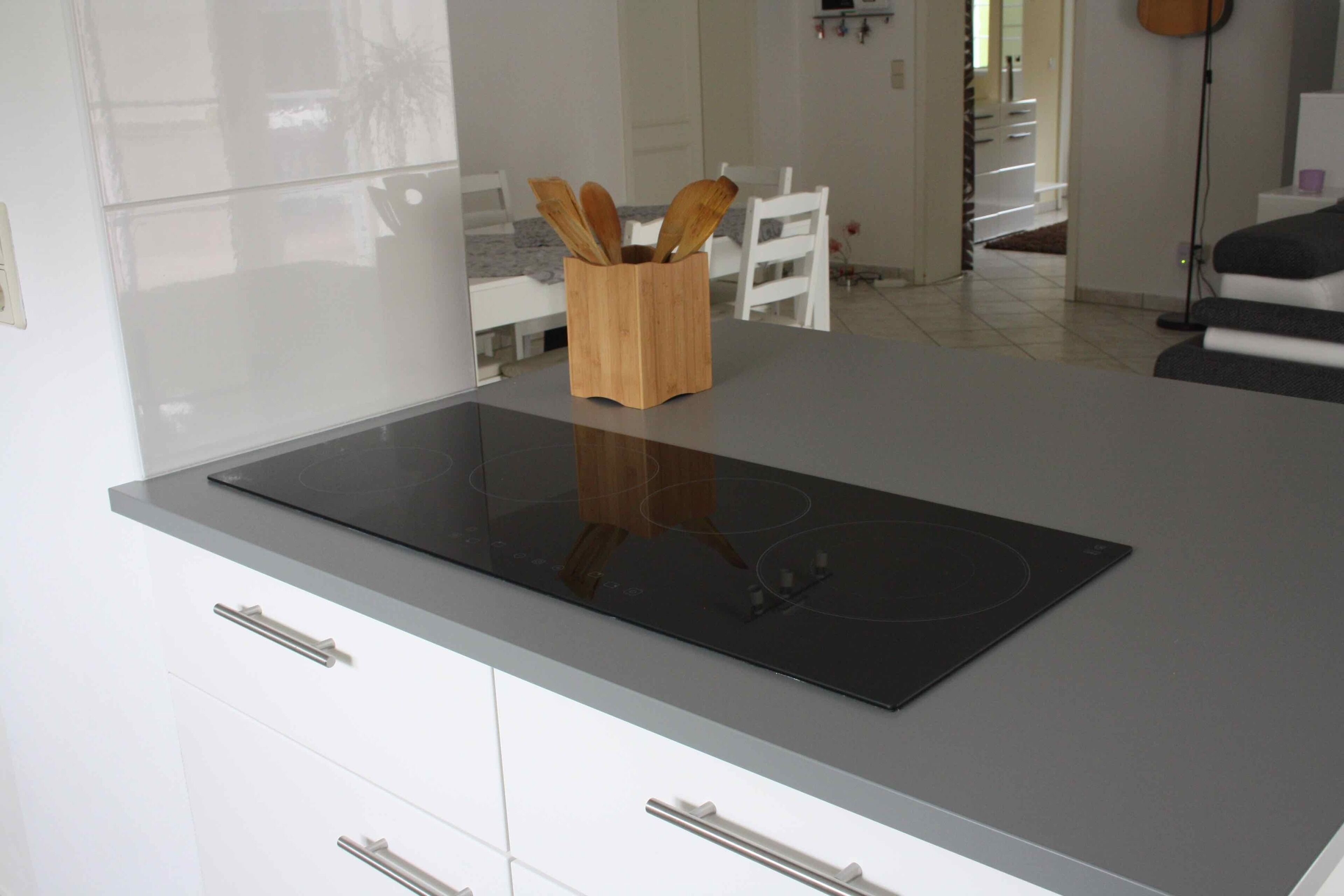 Eine moderne Küche mit einem eleganten schwarzen Induktionskochfeld, weißen Schränken und einem Holz-Utensilienhalter auf der Arbeitsplatte.