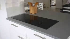 Une cuisine moderne dotée d’une élégante plaque de cuisson à induction noire, de meubles blancs et d’un porte-ustensiles en bois posé sur le plan de travail.