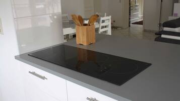 Eine moderne Küche mit einem eleganten schwarzen Induktionskochfeld, weißen Schränken und einem Holz-Utensilienhalter auf der Arbeitsplatte.