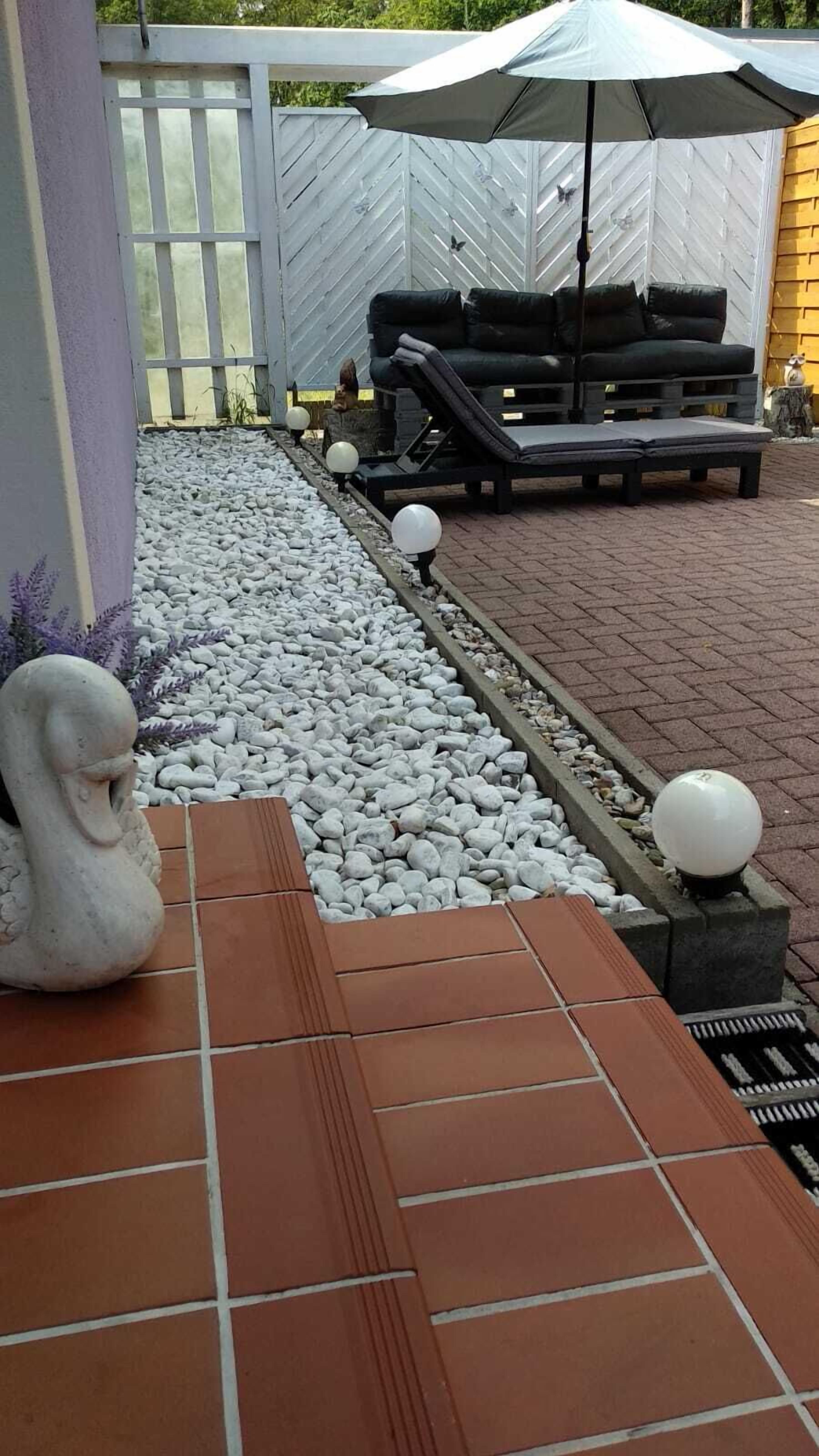 Eine Terrasse mit Sitzgelegenheit, einer dekorativen Steinskulptur und einem mit Kieselsteinen und Fliesen ausgelegten Weg.