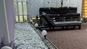 Un espace patio aménagé avec des sièges, une sculpture en pierre décorative et un chemin bordé de galets et de carreaux.