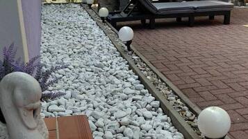 Eine Terrasse mit Sitzgelegenheit, einer dekorativen Steinskulptur und einem mit Kieselsteinen und Fliesen ausgelegten Weg.