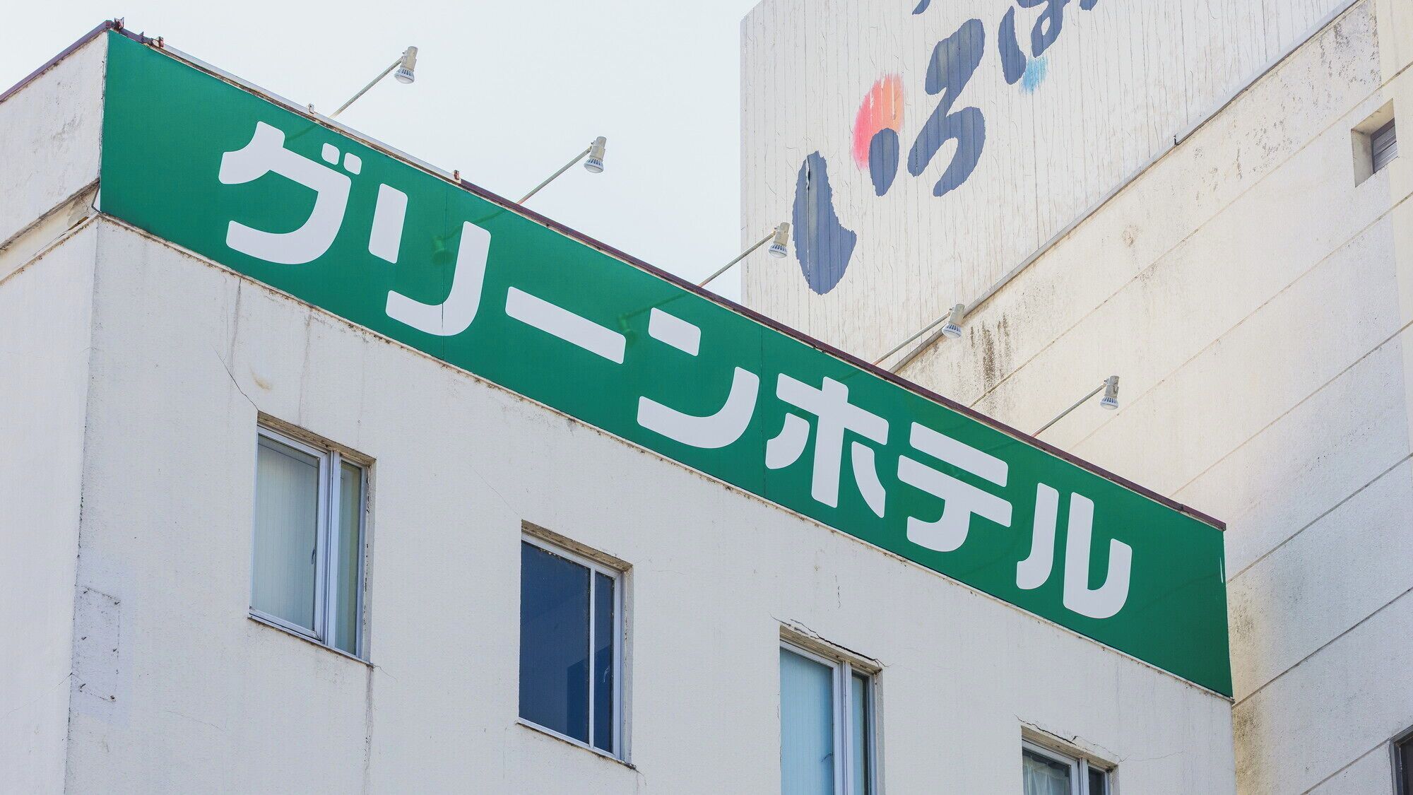 Un bâtiment avec une enseigne verte sur laquelle on peut lire « グリーンホテル » (Green Hotel).