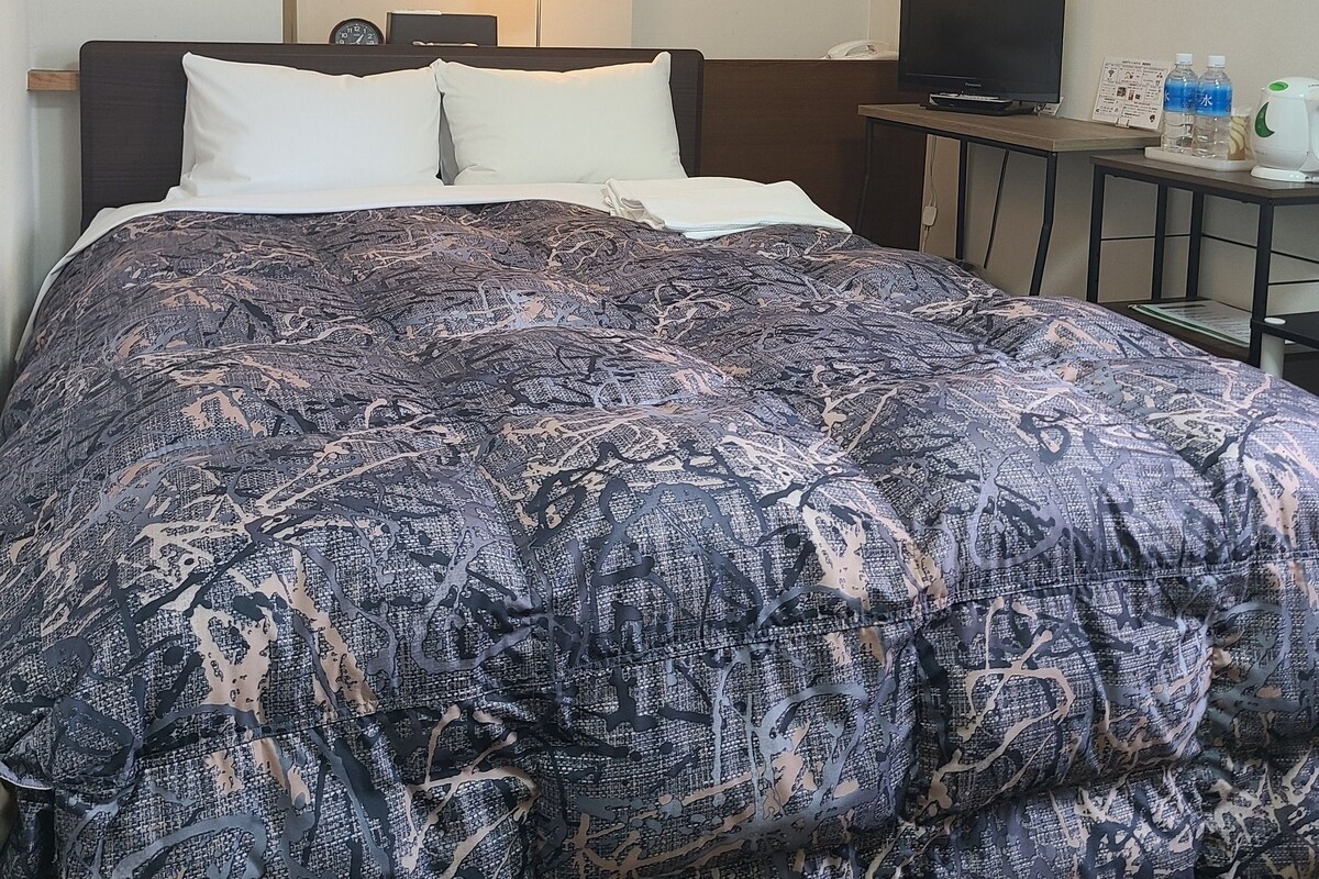 Ein Hotelzimmer mit Bett, Fernseher, Lampe und einem kleinen Tisch mit Wasserkocher und Wasserflaschen.