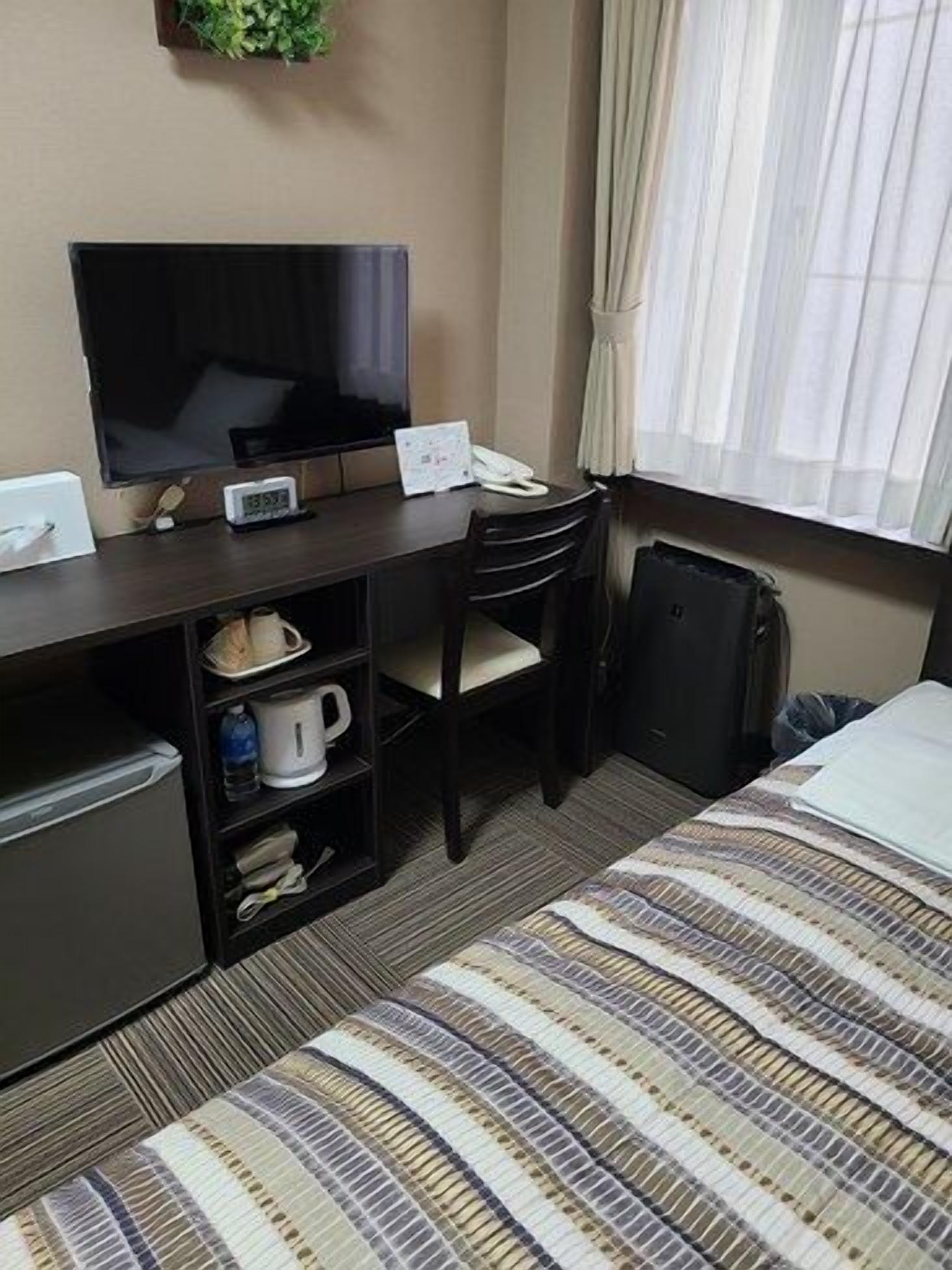 A hotel room with a bed, a desk with a TV, a small fridge, a coffee maker, and a suitcase.