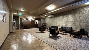 A lobby with a reception desk, seating area, and a brick wall. - Mizusawa Green Hotel (Oshu)