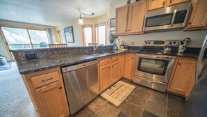 A kitchen with granite countertops, stainless steel appliances, wooden cabinets, and a large window.