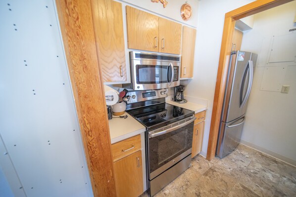 A compact kitchen with wooden cabinets, a stainless steel microwave, oven, and refrigerator. - Keystone Lake Studio | Balcony & Pool Access (Keystone)