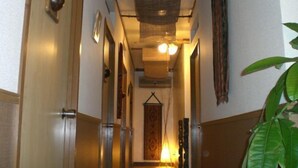 A narrow hallway with a hanging lantern, a door on the left, and a plant on the right. - Guesthouse Sea Pappa (Naha)
