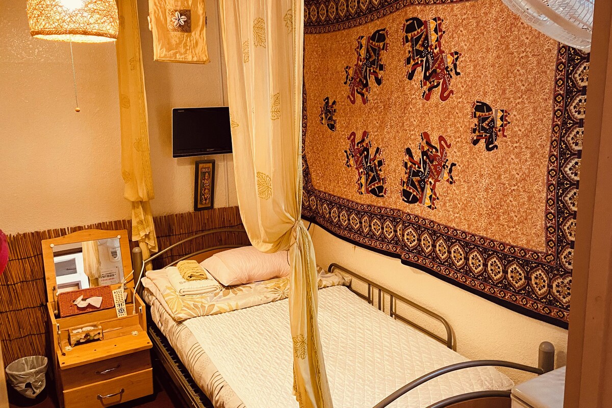 Une chambre avec un lit, une table de chevet, une tapisserie murale, un téléviseur et un rideau.