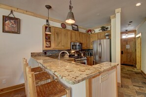 Eine Küche mit Holzausstattung, Granit Arbeitsplatten und Edelstahlgeräten, darüber eine Pendelleuchte.