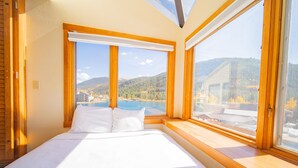 Une chambre avec un grand lit, des fenêtres en bois et une vue sur un lac et des montagnes.