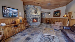 Ein gemütliches Wohnzimmer mit Kamin aus Stein, Holzmöbeln und einem an der Wand montierten Fernseher.