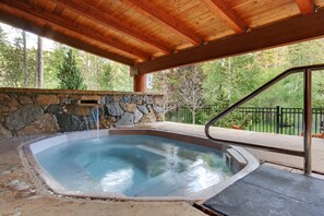 Un jacuzzi bajo una pérgola de madera con un muro de piedra de fondo y vistas a árboles.