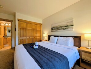 A hotel room with a large bed, wooden wardrobe, a painting on the wall, and a nightstand with a lamp.