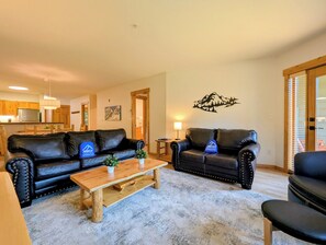 A living room with two black leather sofas, a wooden coffee table, and a mountain-themed wall decal.