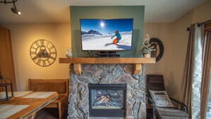 Una sala de estar acogedora con una chimenea de piedra, un televisor montado encima y una decoración de pared con temática de esquí.