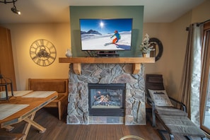 Un salon chaleureux avec une cheminée en pierre, un téléviseur fixé au-dessus et une décoration murale sur le thème du ski.