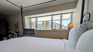Un lit bien fait dans une chambre d’hôtel, avec une grande fenêtre donnant sur un paysage de arbres et de montagnes.