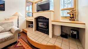 A living room with a fireplace, a sofa, a lamp, and a television mounted above the fireplace. - Quiet Condo w/Mtn Views, Private Laundry & Shuttle (Keystone)