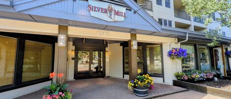 Ein Hotel mit Eingangsbereich und einem Schild, auf dem 'Silver Mill' und die Adresse '0140' steht. Vor dem Eingang befinden sich Blumenkästen.