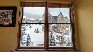 A window with a view of a snowy landscape and a building with a pointed roof. - Cozy Summer Retreat – Views, Hot Tub & River Run (Keystone)