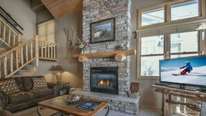 Una sala de estar acogedora con chimenea de piedra, televisor y una escalera.