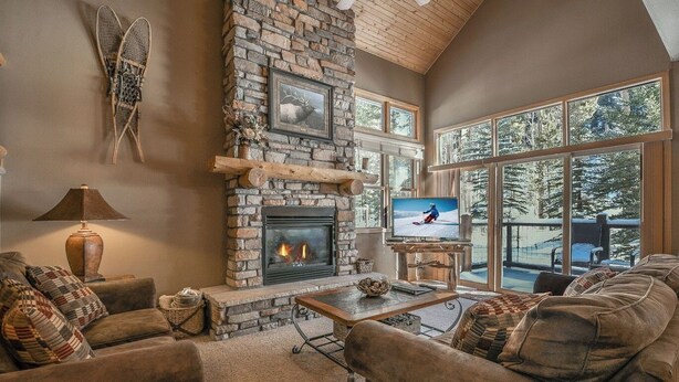 Una sala de estar acogedora con chimenea de piedra, televisor y un ventanal con vistas a un paisaje nevado.