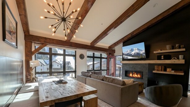 A cozy living room with a fireplace, a television, and a large window overlooking a snowy mountain. - Ultra-Luxury Penthouse | 100Yds to Slopes (Keystone)