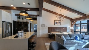 A modern kitchen with a central island, bar stools, and a dining area with a wooden table and bench. - Ultra-Luxury Penthouse | 100Yds to Slopes (Keystone)