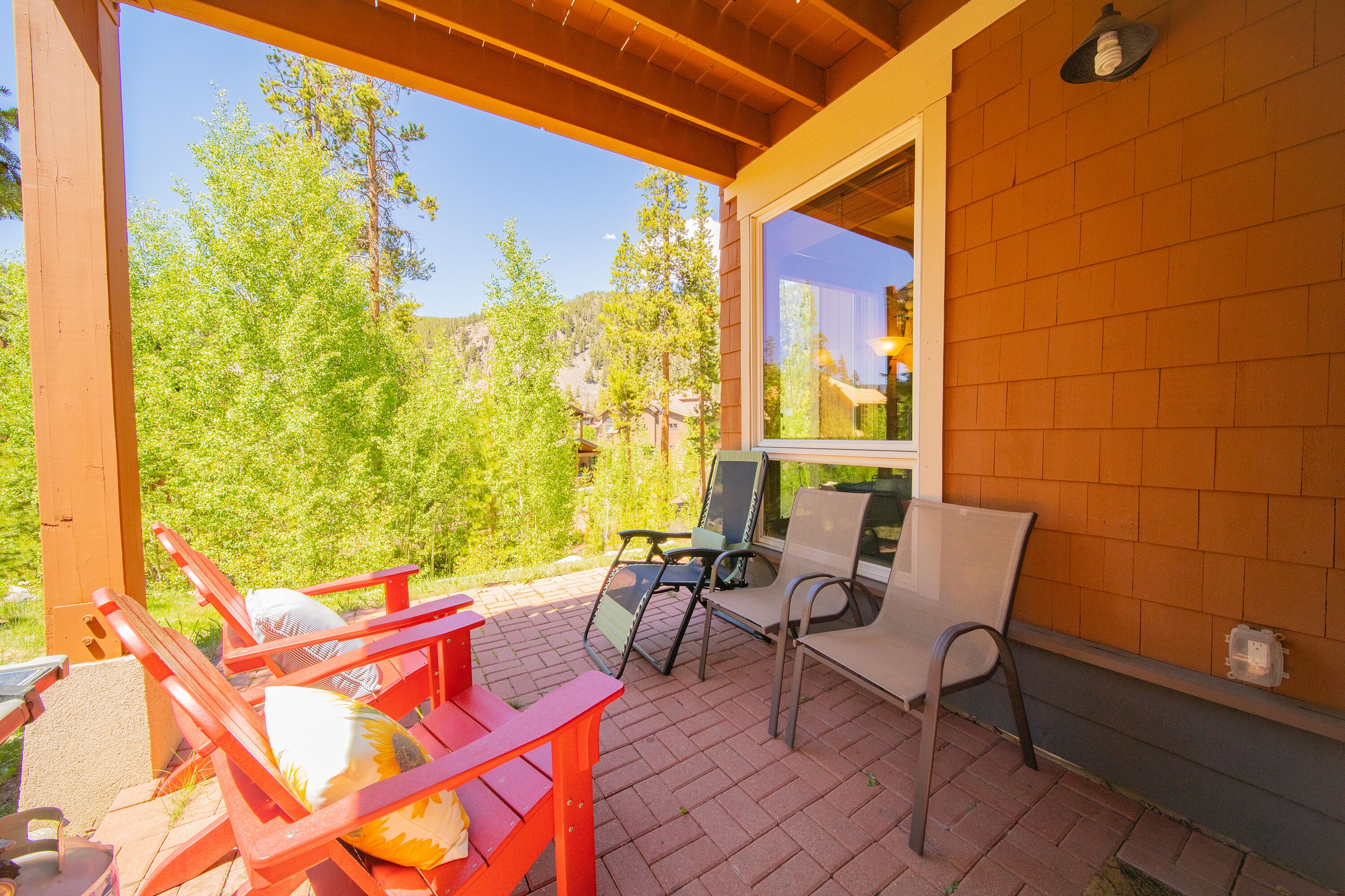 Un patio techado con mobiliario exterior, suelo de ladrillo y vistas a árboles y colinas.