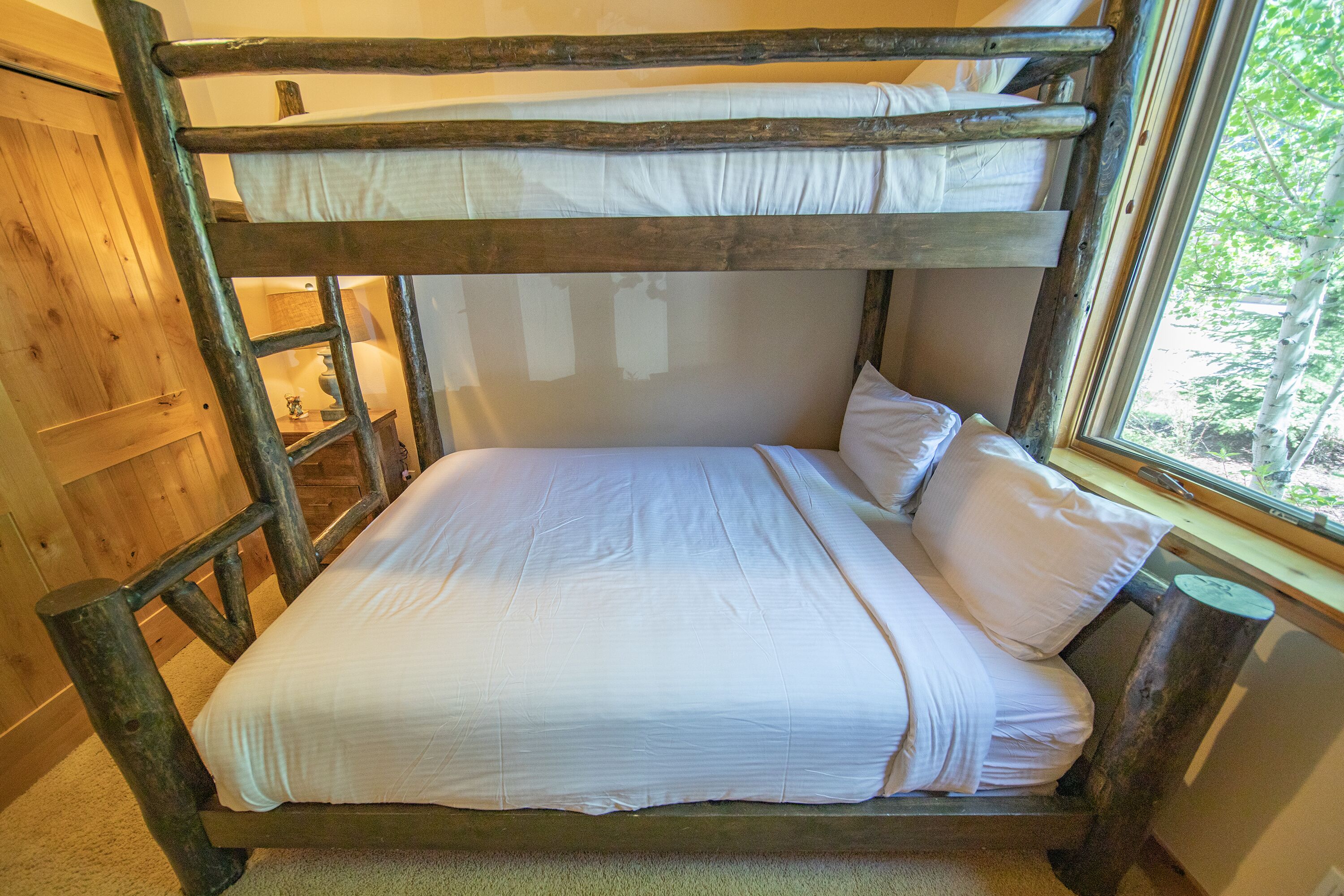 A bunk bed with white bedding and a window with a view of trees.
