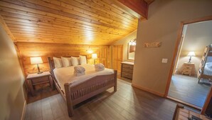 A cozy bedroom with a wooden ceiling, a bed with pillows, two bedside tables with lamps, and a mirror on the wall. - Family-Friendly Escape | Balcony & Bike Path (Keystone)