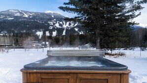 Un jacuzzi de madera en un paisaje nevado con montañas al fondo.
