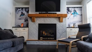 A modern living room with a fireplace, a flat-screen TV mounted above it, and two armchairs.
