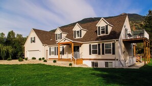 A large, two-story house with a covered porch and a deck, surrounded by a well-maintained lawn and trees.