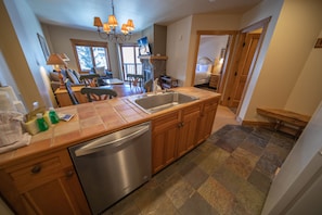 A kitchen with a dishwasher, wooden cabinets, a sink, and a dining area with chairs and a table.