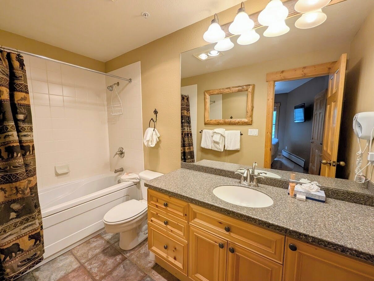 A bathroom with a bathtub, toilet, vanity with a sink, and a large mirror.